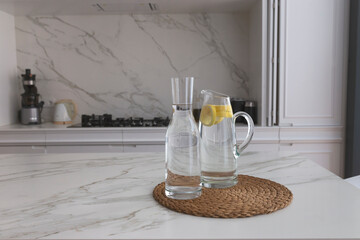 Jugs full of water with lemon on a marble countertop of an elegant kitchen placed on a wicker tray