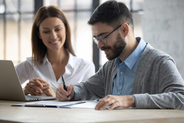 Customer and mortgage consultant in office. Male client signing loan agreement at desk with...