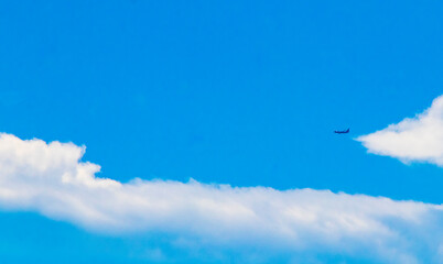 Passenger airplane flies in blue sky with clouds in Mexico.