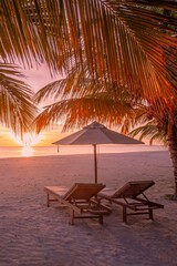Beautiful tropical sunset coast, two sun beds chairs umbrella under palm trees. Closeup white sand,...