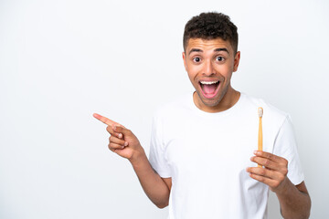 Young Brazilian man brushing teeth isolated on white background surprised and pointing finger to the side