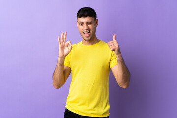 Young Colombian man isolated on purple background showing ok sign and thumb up gesture