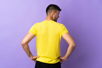 Young Colombian man isolated on purple background in back position and looking side