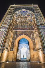 Facade of the Gur Emir mausoleum with mosaics and brick walls at night with illumination in the ancient city of Samarkand in Uzbekistan, oriental architecture in the evening
