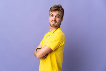 Young handsome blonde man isolated on purple background with arms crossed and happy