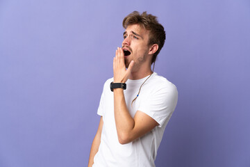Young handsome blonde man isolated on purple background yawning and covering wide open mouth with...