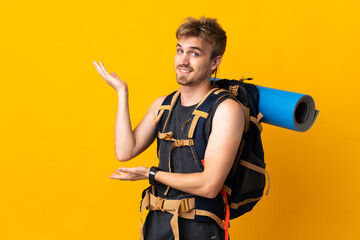 Young mountaineer man with a big backpack isolated on yellow background extending hands to the side...