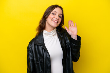 Young caucasian woman isolated on yellow background saluting with hand with happy expression