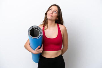 Young sport caucasian woman going to yoga classes while holding a mat isolated on white background and looking up