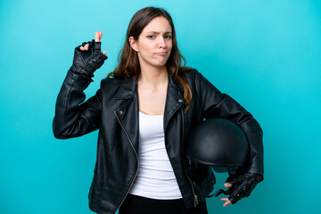 Young caucasian woman with a motorcycle helmet isolated on blue background with fingers crossing and wishing the best