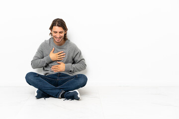 Young handsome man sitting on the floor over isolated background smiling a lot