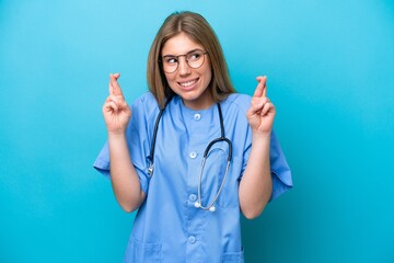 Young surgeon doctor woman isolated on blue background with fingers crossing