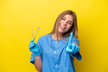 Dentist caucasian woman holding tools isolated on yellow background showing and lifting a finger
