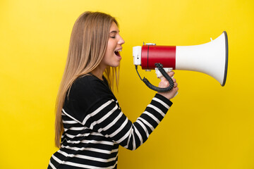 Young caucasian woman isolated on yellow background shouting through a megaphone to announce...