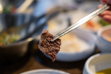 Chopsticks holding a piece of Hanwoo, Korean Style Grilled Meat. BBQ meat with soft focus