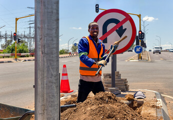 african american worker with a pickaxe digging a ditch in the highway to repair cabling on an isle...