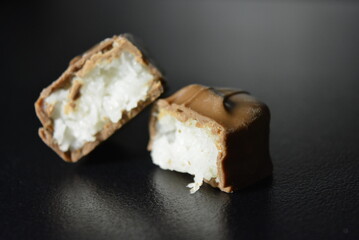 Pieces, slices of sweet coconut bar covered with milk chocolate placed on a black background.