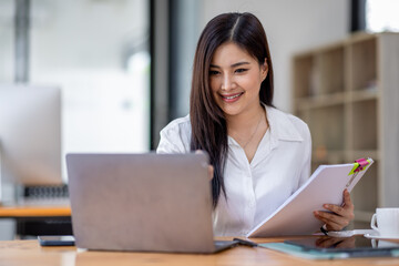 Asian Businesswoman Using laptop computer and working at office with calculator document on desk, doing planning analyzing the financial report, business plan investment, finance analysis concept.
