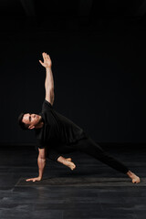  A beautiful youth, clad in dark clothing, engages in the art of yoga on a mat, embodying strength and flexibility as he moves through captivating asanas.