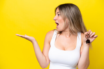 Young Rumanian woman holding home keys isolated on yellow background with surprise facial expression