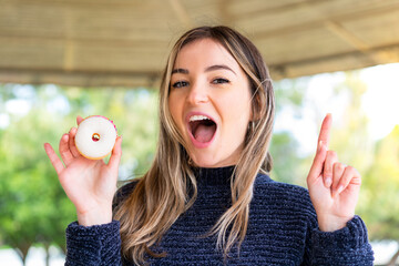 Young pretty Romanian woman holding a donut at outdoors pointing up a great idea