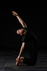 The handsome young man, draped in black, transitions seamlessly through a symphony of yoga poses on...