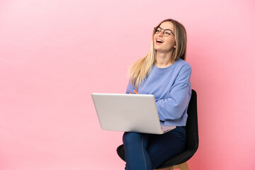 Young woman sitting on a chair with laptop over isolated pink background happy and smiling