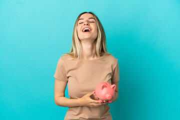 Young woman holding a piggybank over isolated blue background laughing