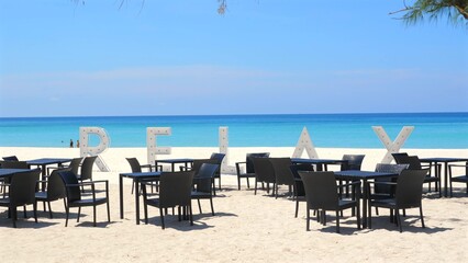 Tropical beach restaurant with RELAX sign set up on white sand facing serene ocean. Idyllic vacation spot for dining and unwinding. Leisure travel and tourism.