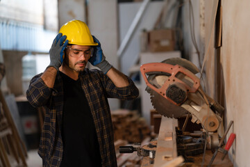 Young carpenter wearing earmuffs before cutting wood plank by circular saw machine at carpentry shop, security protection. Joiner, builder, maker of furniture handmade at workshop