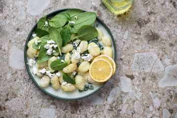 Plate with spanakopita gnocchi on a light-brown granite background, horizontal shot with space, view from above