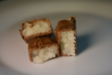 Pieces, slices of sweet coconut bar covered with milk chocolate placed on a white glass plate.