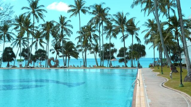 Tropical resort view with large swimming pool surrounded by palm trees and sun loungers, inviting relaxation and leisure by sea. Vacation and travel destinations.