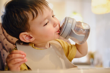 Baby boy drinks water from a bottle of non-spill bottle in a cafe. A child eats in a restaurant...