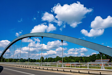 Fototapeta premium Bridge spans over highway against blue sky filled with white clouds