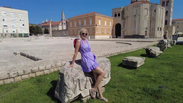 Elegant lady with hat in the Ancient Roman square of Zadar of Croatia, capital of Dalmatia. Old Roman Forum with Cathedral of St. Anastasia and Church of St Donatus with the bell tower.