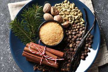 Plate with different aromatic spices and fir branches on grey textured table, top view