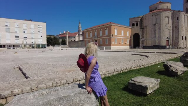 Elegant lady with hat in the Ancient Roman square of Zadar of Croatia, capital of Dalmatia. Old Roman Forum with Cathedral of St. Anastasia and Church of St Donatus with the bell tower.
