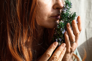 Redhead Woman holding in her hands a bunch of blooming rosemary and inhales it's scent. Herbalist woman preparing fresh organic herbs for natural herbal methods of treatment. Alternative medicine. © Caterina Trimarchi
