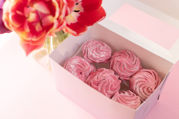 Pink marshmallow lies in a gift box near a vase with tulips on a pink background