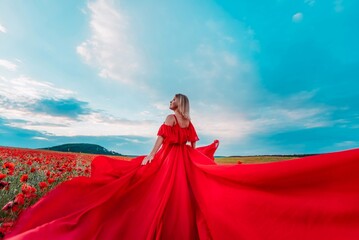 Fototapeta premium Woman poppy field red dress. Happy woman in a long red dress in a beautiful large poppy field. Blond stands with her back posing on a large field of red poppies