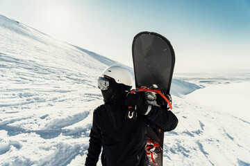 A snowboarder in black attire holds a board, gazing over a pristine snowy slope, the thrill of the...