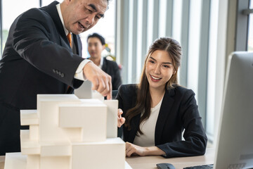 Young Asian woman presents a building model to boss at the office. They discuss building design together in the office.