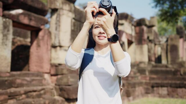 A smiling woman traveler with a backpack taking photos of ancient ruins, immersed in the experience of discovery.