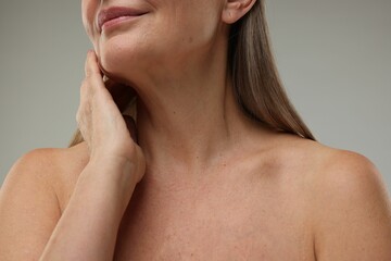 Mature woman touching her neck on grey background, closeup