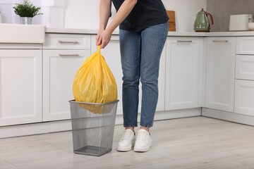 Woman taking garbage bag out of trash bin in kitchen, closeup