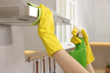 Woman with spray bottle and microfiber cloth cleaning kitchen hood indoors, closeup