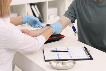 Doctor taking blood sample from patient with syringe at white table in hospital, closeup