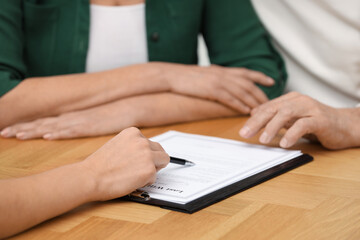 Notary showing senior couple where to sign Last Will and Testament at wooden table, closeup