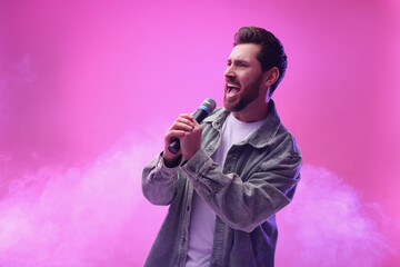 Handsome man with microphone singing on pink background. Space for text